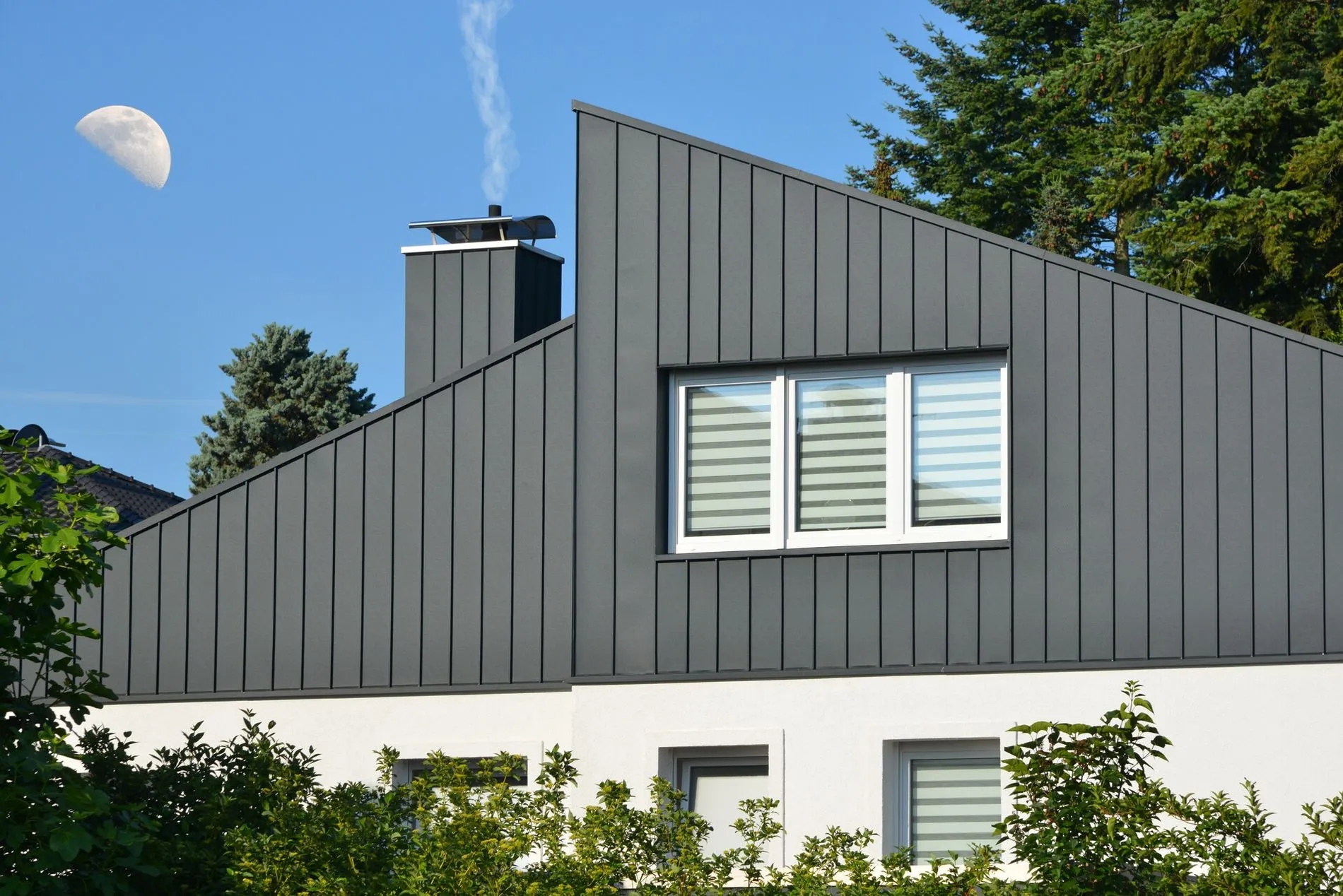 Fassaden- und Schornstein-Verkleidung eines modernen WohngebÃ¤udes aus dunkelgrau beschichtetem Stehfalz-Metall und Fenster mit Sichtschutzstreifen, .jpg