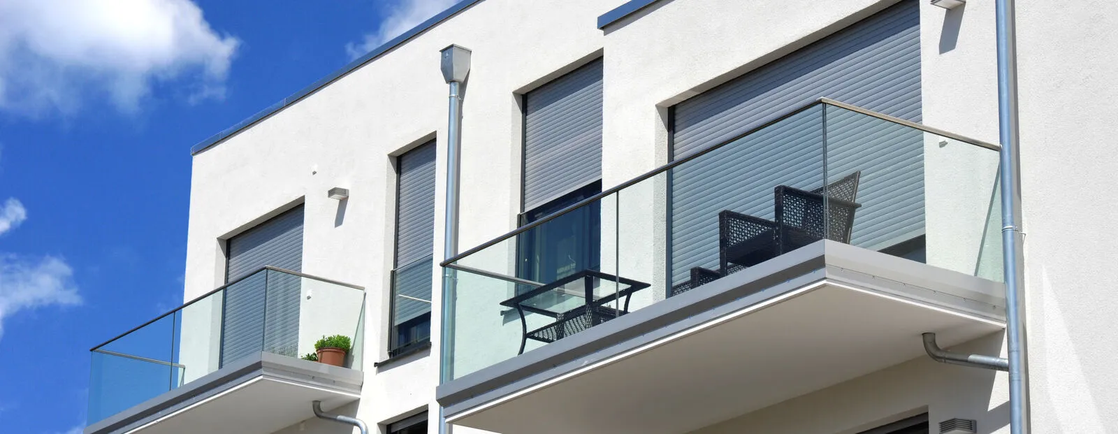 Moderne Balkone, verglast mit Metall-GelÃ¤nder an Neubau-Hausfront mit Flachdach, WasserkÃ¤sten, Regenfallrohren und Edelstahl-Attika.jpg